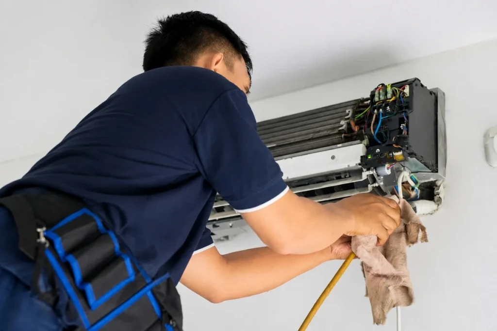 Technician performing mini split maintenance on an indoor wall mounted AC unit.